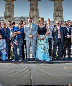A large group of people posing for a photo in front of ancient columns at a historical site. - Olive Oil Times
