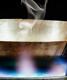 Metal cooking pan with steam rising above it on a gas stove with a blue flame. - Olive Oil Times