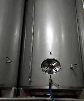 Three stainless steel fermentation tanks with circular openings and valves. - Olive Oil Times