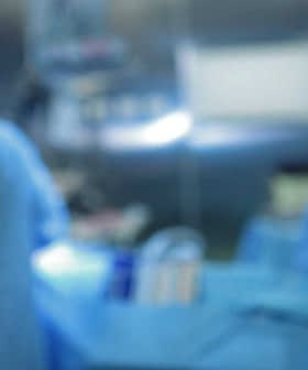 Two medical professionals wearing scrubs and masks working in an operating room with surgical instruments. - Olive Oil Times