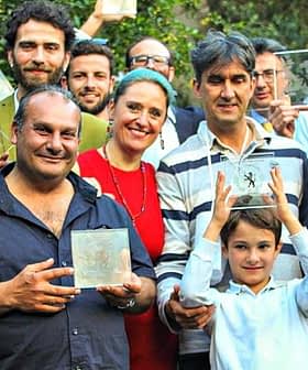 A group of individuals holding glass awards, posing together outdoors in a celebratory manner. - Olive Oil Times