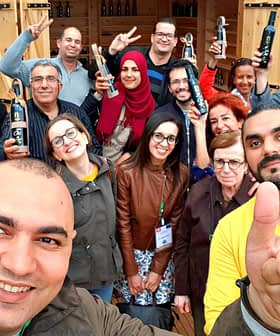 Group of people posing for a photo, some holding olive oil bottles, with smiles and gestures. - Olive Oil Times