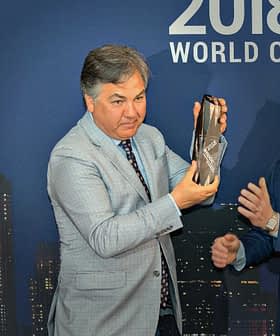 Two men at an award ceremony, one presenting a bottle to the other in front of a city skyline backdrop. - Olive Oil Times