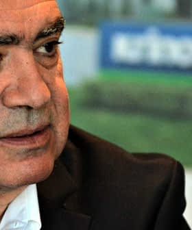 Man with gray hair wearing a black suit and white shirt, seated and looking to the side. - Olive Oil Times