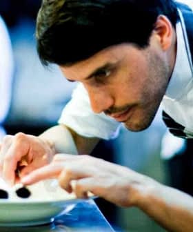Chef carefully plating food on a white plate in a professional kitchen setting. - Olive Oil Times