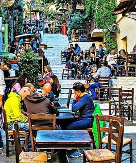 Outdoor dining area featuring wooden tables and chairs in a bustling setting with patrons. - Olive Oil Times