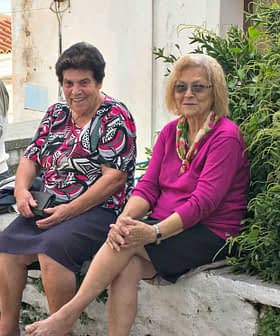Five elderly individuals sitting on a stone wall in a village setting, with greenery in the background. - Olive Oil Times