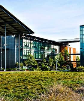 Modern building featuring a combination of glass and orange exterior elements with a landscaped area in front. - Olive Oil Times
