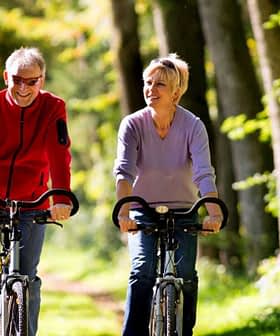 A man and woman riding bicycles side by side on a tree-lined path during daylight. - Olive Oil Times