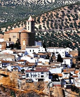 A panoramic view of a white village in Andalusia surrounded by olive groves on rolling hills. - Olive Oil Times