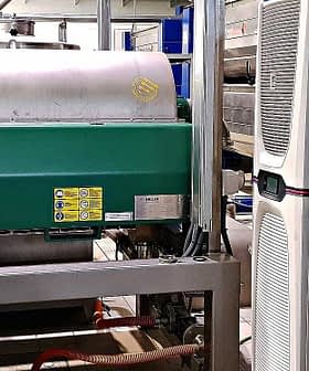 Industrial machinery used for olive oil processing, featuring a green motor and stainless steel tanks. - Olive Oil Times