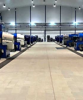 Row of industrial olive oil processing machines in a large facility with blue and gray colors. - Olive Oil Times