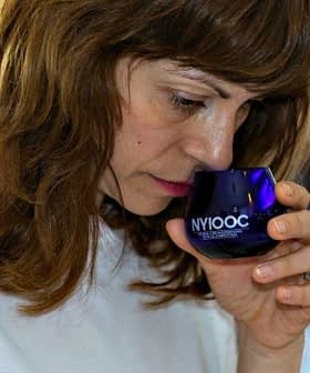 Woman with brown hair smelling olive oil from a blue glass container during a tasting event. - Olive Oil Times