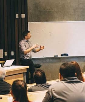 A speaker presenting in front of an audience in a classroom with a whiteboard. - Olive Oil Times