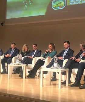 A panel of speakers seated on stage during a conference event, discussing various topics. - Olive Oil Times