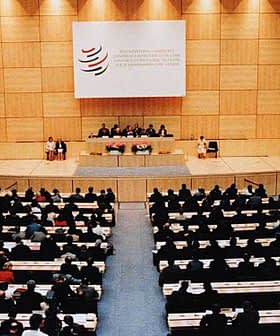 Interior view of a large conference hall during a World Trade Organization meeting with attendees seated. - Olive Oil Times