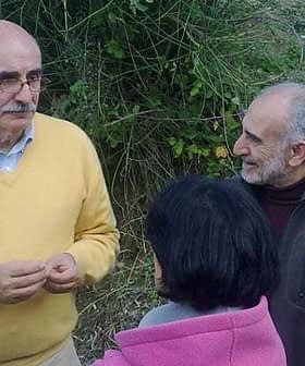A man wearing a yellow sweater speaking to a small group of people outdoors. - Olive Oil Times