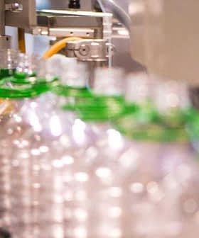 A production line with clear plastic bottles being filled with olive oil at a bottling facility. - Olive Oil Times