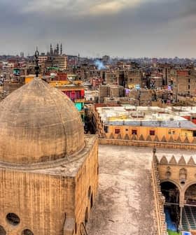View of a historic mosque dome with a cityscape of Cairo in the background during sunset. - Olive Oil Times