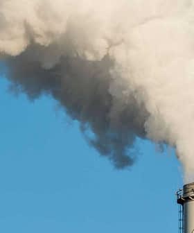 Two industrial smoke stacks releasing white vapor into a clear blue sky. - Olive Oil Times