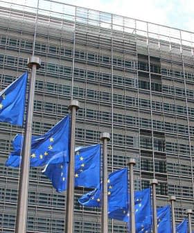 Multiple European Union flags displayed in front of a modern glass building. - Olive Oil Times