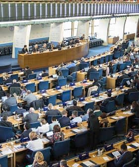 View of a legislative assembly hall with rows of seats and a central podium filled with representatives. - Olive Oil Times
