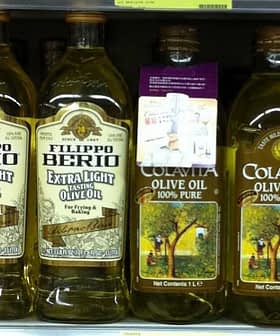Various bottles of olive oil displayed on a supermarket shelf, including Filippo Berio and Colavita brands. - Olive Oil Times