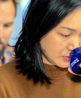 Woman with black hair holding a blue glass to her lips while tasting. - Olive Oil Times