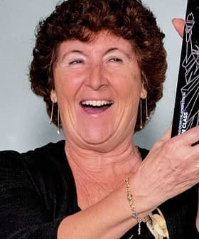 A woman with curly hair smiling while holding a black award trophy in her hands. - Olive Oil Times