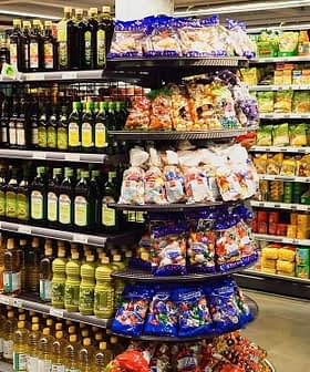 A grocery store aisle featuring shelves stocked with various olive oil bottles and snack items. - Olive Oil Times