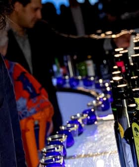 Man in a dark suit looking at a row of various bottles on a bar at an event. - Olive Oil Times