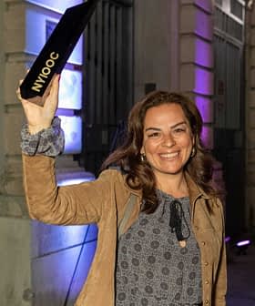 A woman smiling and holding a black award while standing outdoors at night. - Olive Oil Times