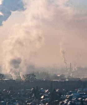 Smoke rising from industrial chimneys in an urban area with a hazy sky. - Olive Oil Times