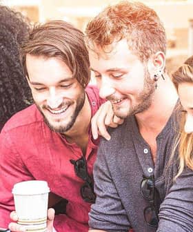 A group of six friends sitting together, looking at mobile devices and smiling. - Olive Oil Times