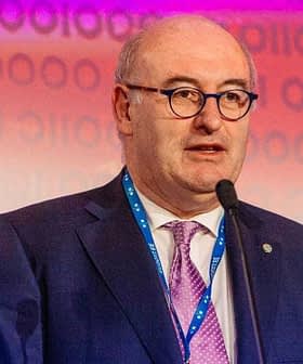 Phil Hogan speaking at a podium during an event with a microphone in front of a colorful background. - Olive Oil Times