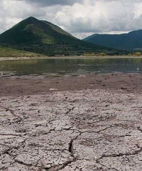 Dry, cracked earth with a mountain in the background under a cloudy sky. - Olive Oil Times