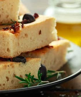 Slices of focaccia bread topped with olives and herbs on a black plate. - Olive Oil Times