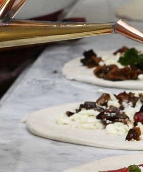 A copper oil dispenser pouring extra virgin olive oil onto a pizza base with toppings. - Olive Oil Times
