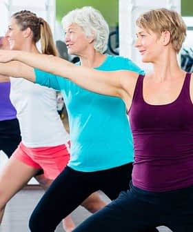Four adults performing a fitness exercise in a gym setting with arms extended. - Olive Oil Times