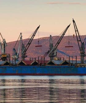 Cargo ship docked at the port of Volos with cranes and a tugboat nearby. - Olive Oil Times