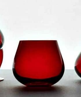 Three pieces of red glassware including a curved glass, a round glass, and a tilted glass. - Olive Oil Times