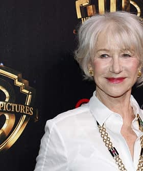 Woman with short gray hair wearing a white shirt and necklace at a Warner Bros. Pictures event backdrop. - Olive Oil Times