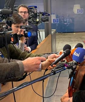 A woman speaking to reporters while being filmed by multiple cameras in a press setting. - Olive Oil Times