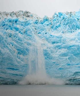 A large glacier with a waterfall cascading down its icy surface into the water below. - Olive Oil Times