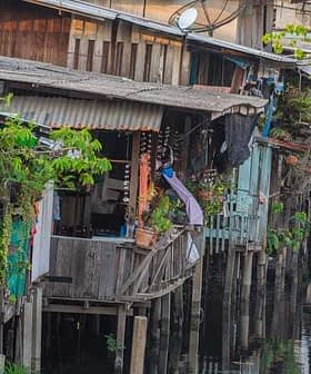Wooden houses on stilts along a waterway, featuring plants and clothes hanging outside. - Olive Oil Times