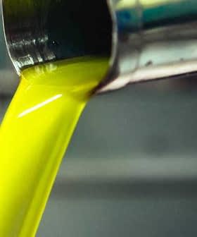 Stream of green olive oil pouring from a metal spout into a container. - Olive Oil Times