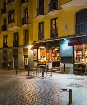 Street view of a yellow building featuring a café with outdoor seating and illuminated signage at night. - Olive Oil Times