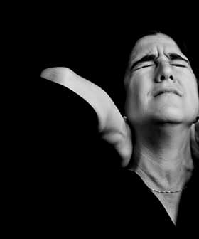 Black and white portrait of a woman with closed eyes and hands on her neck, expressing a moment of contemplation. - Olive Oil Times