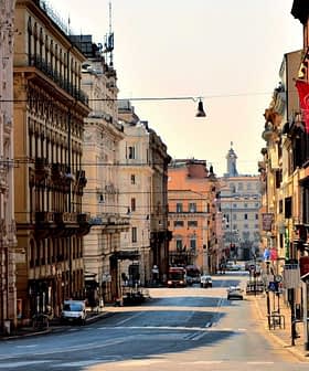 View of a wide, empty street in Rome with buildings lining both sides and traffic signals visible. - Olive Oil Times