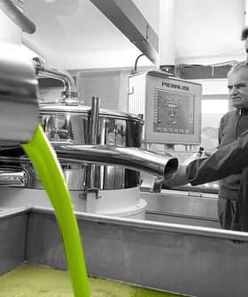 Two men observing the olive oil extraction process in a production facility with green liquid flowing. - Olive Oil Times